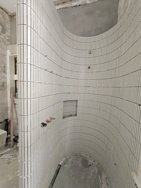 Curved white finger-tile shower wall with a recessed niche